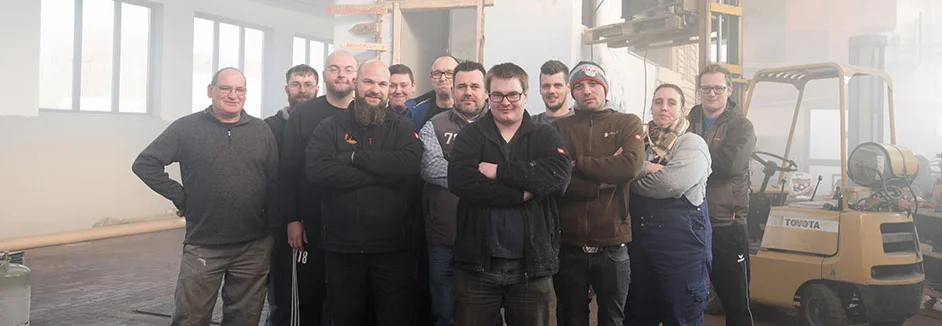 Elf Personen posieren in einer Lagerhalle